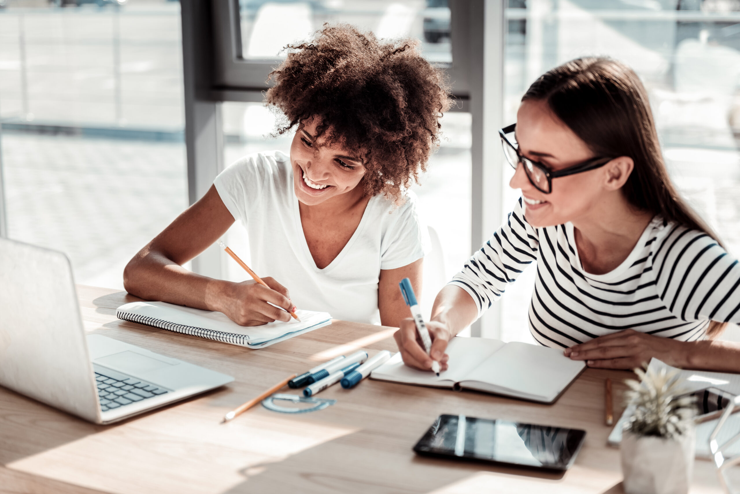 Things to remember. Happy smart nice women looking at the laptop screen and taking notes while working in the office