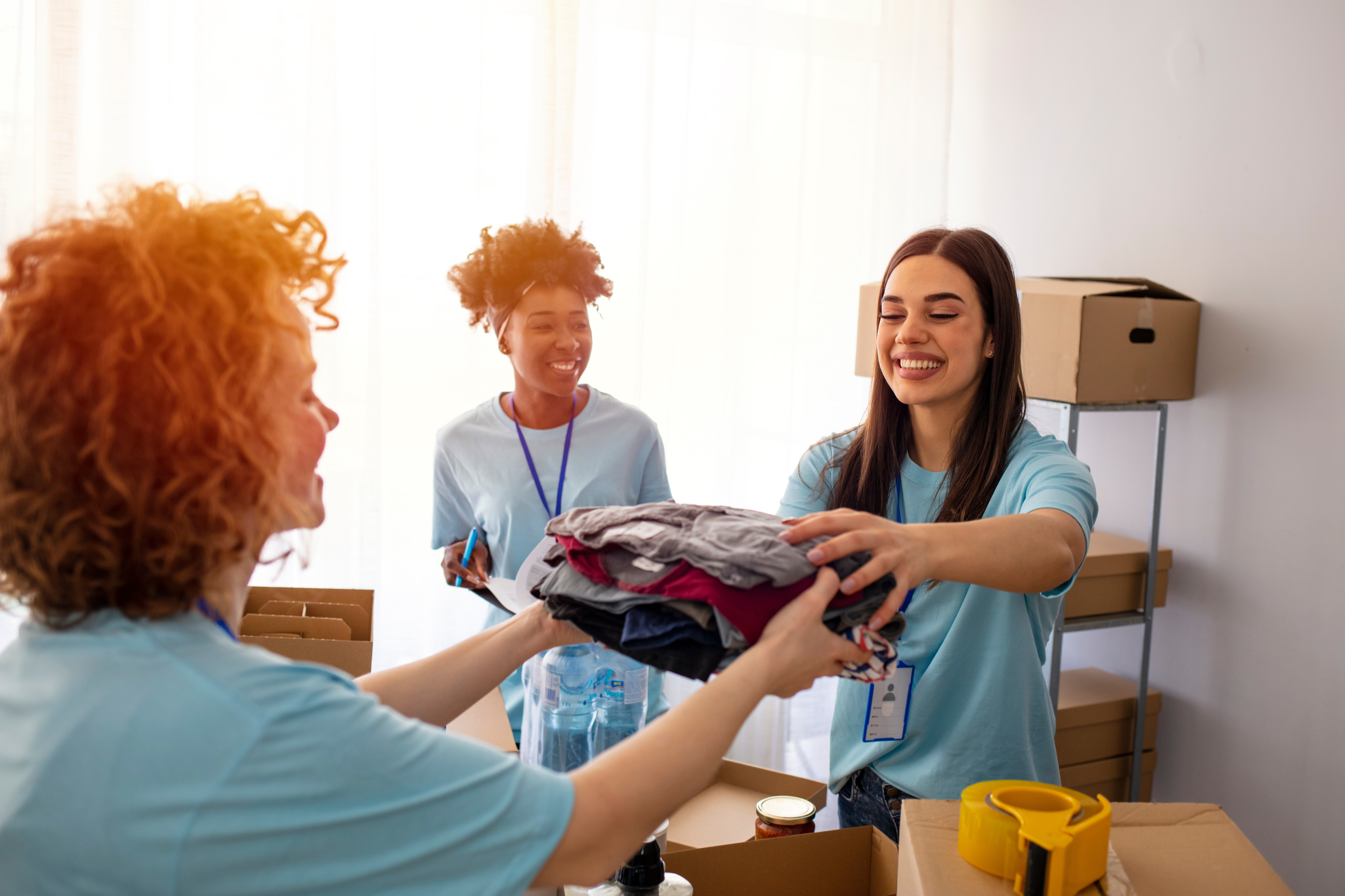 Team of volunteers collecting food donations indoors. Volunteers pack canned goods into boxes during food drive. Helpful team of social workers. Group of mixed race people working in charitable foundation