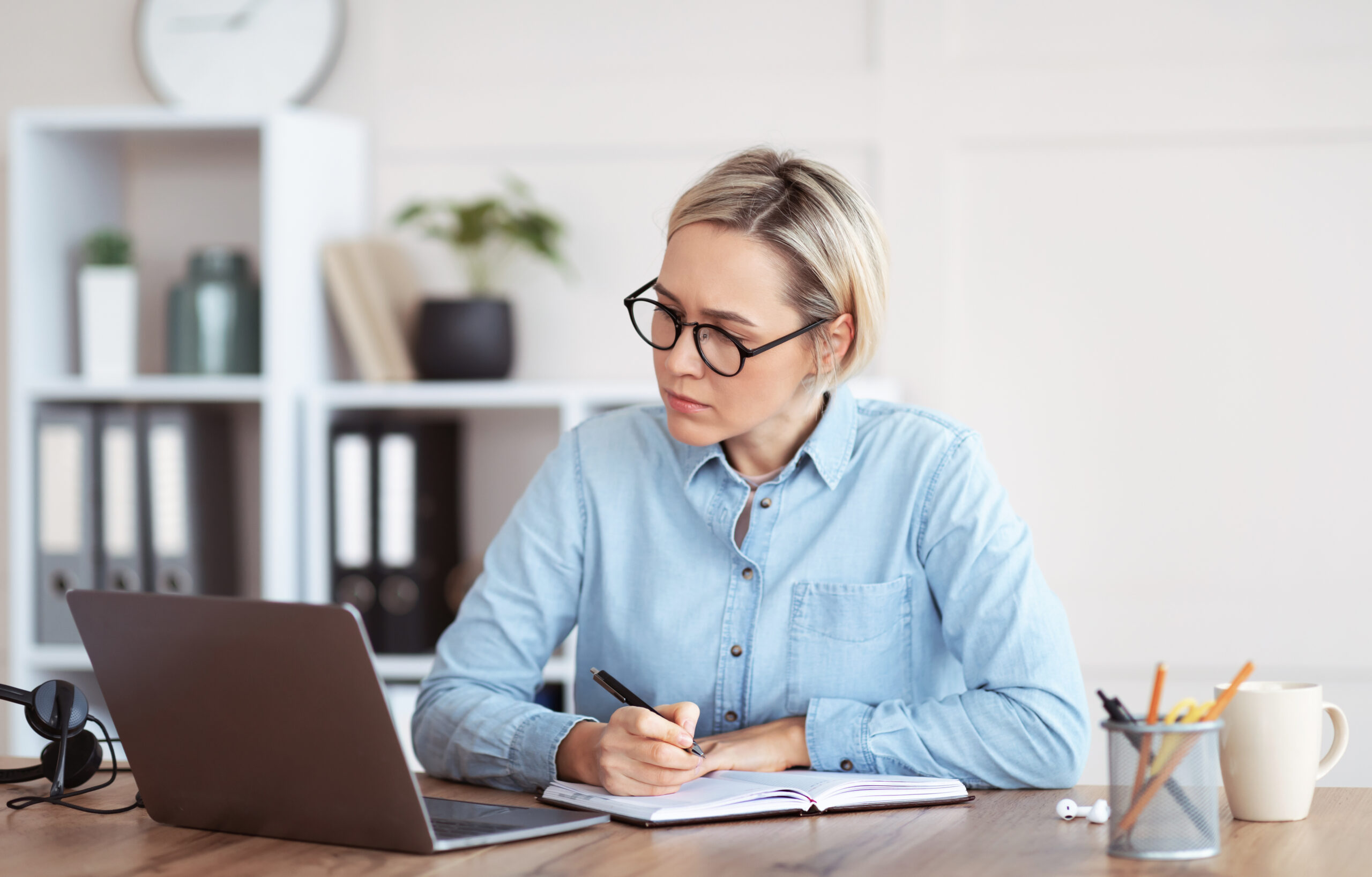 Focused Caucasian woman writing down info during business training or online meeting, participating in web conference from home. Smart female student taking distance training course